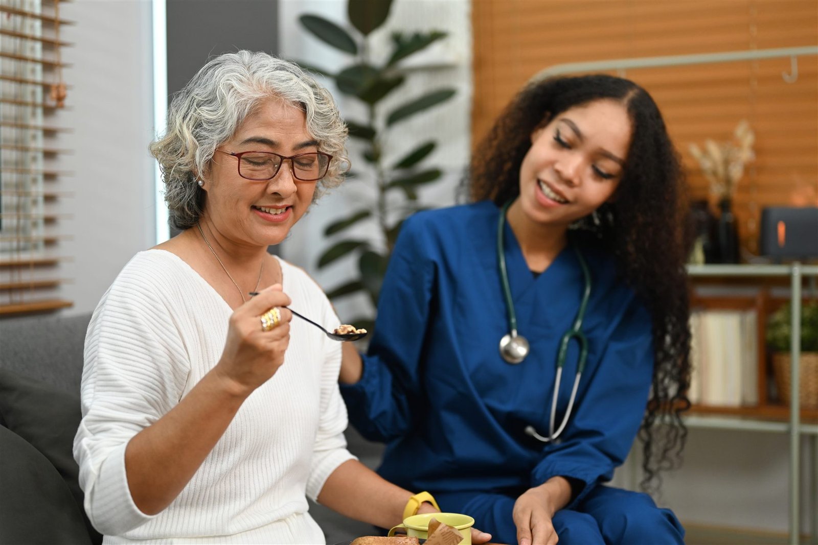 A carer keeping an older lady company at home while she enjoys her breakfast